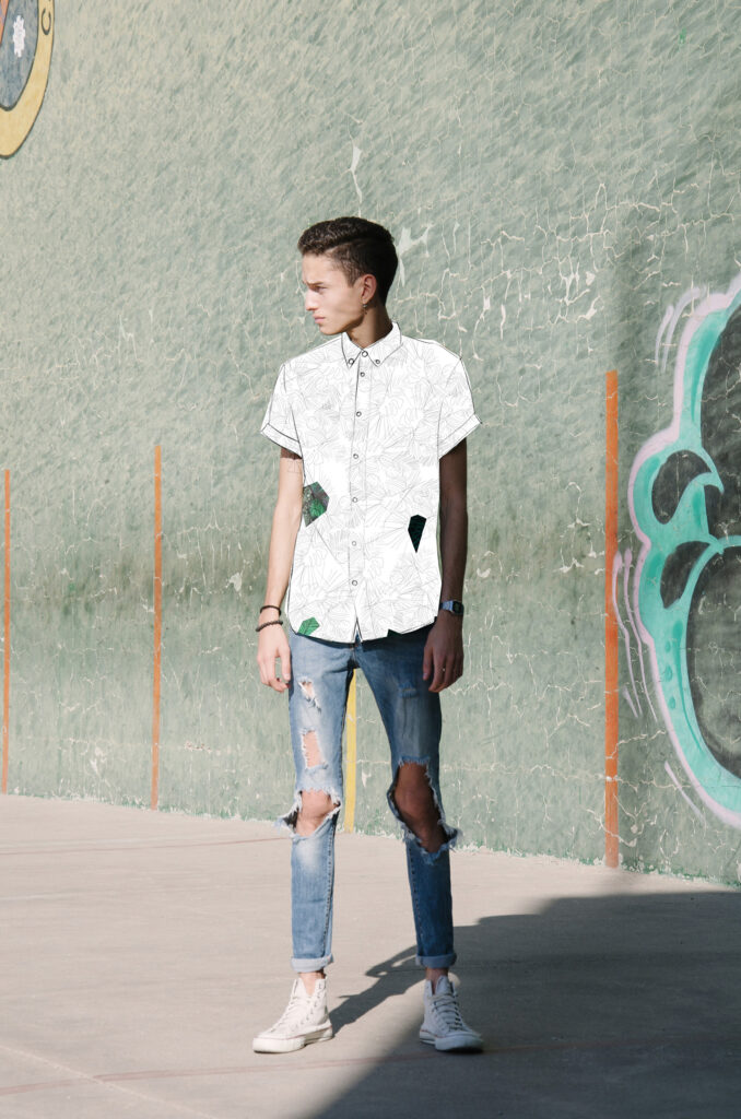 Victor Zepeda stands against a textured green wall adorned with graffiti wearing a white shirt with green patterns distressed blue jeans and white sneakers.